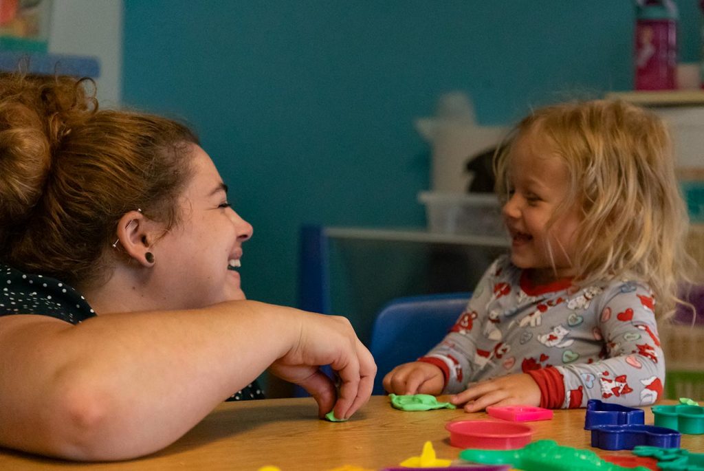 A teacher laughing with a child as they play with playdough