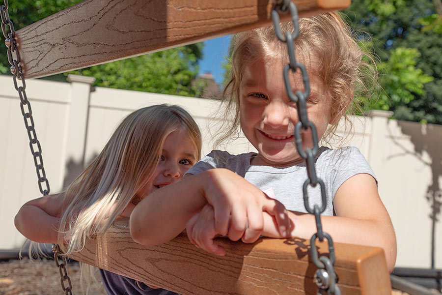Two elementary girls on playground equipment smiling at the camera