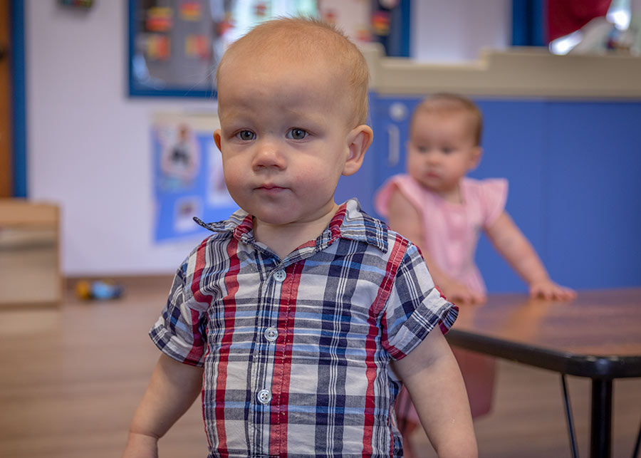 A toddler standing in classroom staring at the camera