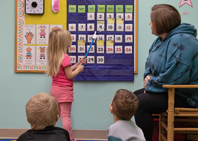 A student pointing to the calendar with the teacher's help